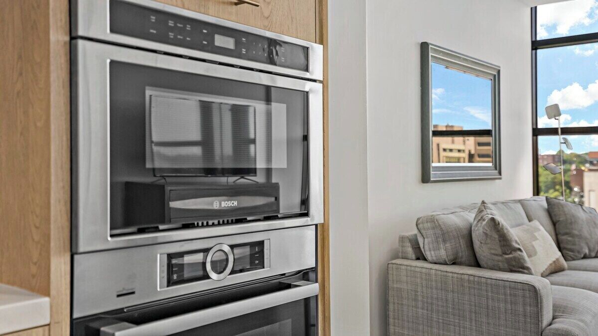 Een compacte keuken met een Bosch oven, een magnetron en een inbouwoven. Er is een raam met uitzicht op gebouwen.