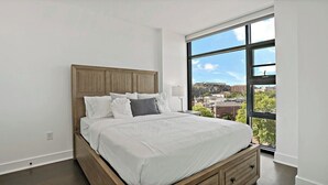 Une chambre moderne dotée d’une grande fenêtre, d’un cadre de lit en bois et offrant une vue sur la ville.