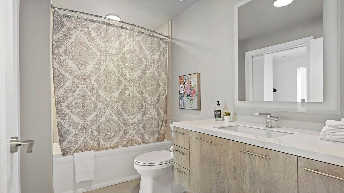 A modern bathroom with a shower curtain, toilet, sink, and wooden cabinets.
