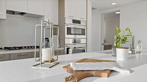 Modern kitchen with stainless steel appliances, white countertop, and a wooden cutting board.