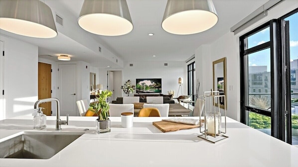 Enjoy a spacious room with a central countertop, sink, and glass container, plus a large window offering a view of the surrounding buildings.