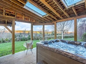 Un jacuzzi bajo una pérgola de madera con vistas a un paisaje cubierto de césped.