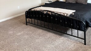 Un dormitorio con un cabecero de metal negro, una alfombra color beige y dos estantes circulares fijos a la pared, adornados con plantas.