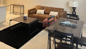 Una sala de estar moderna con un sofá de cuero marrón, una mesa de comedor con sillas, un ventilador de techo y una mesita auxiliar.