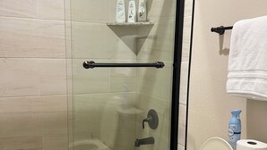 Un baño con ducha de vidrio, inodoro y estante con artículos de tocador.
