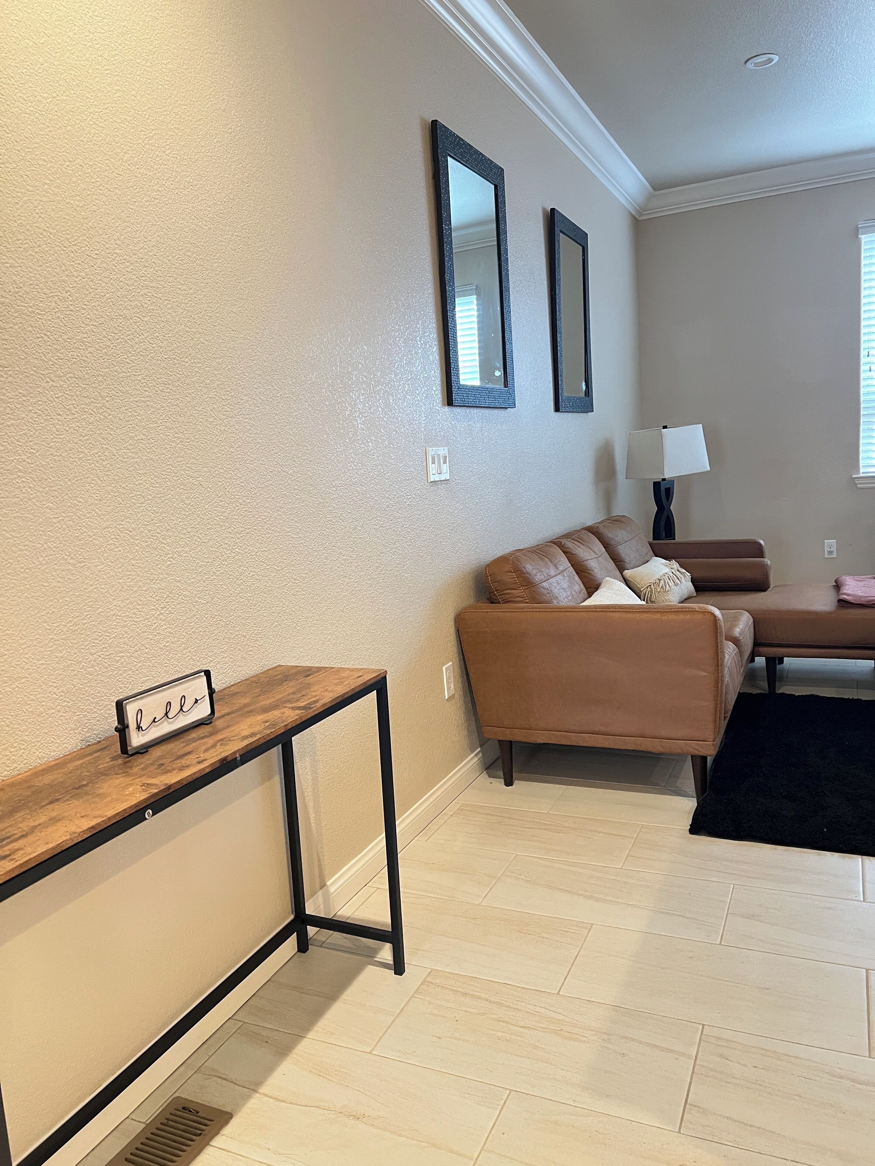 Una sala de estar con un sofá de cuero marrón, una consola de madera con un letrero que dice 'hello', una lámpara de pie negra y un tapete negro.