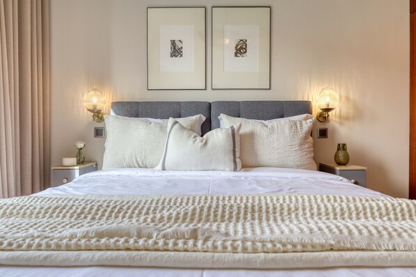 A neatly made double bed with white linens, two wall-mounted lamps, and two framed abstract artworks. - Refúgio no Funchal, a Home in Madeira (Funchal)