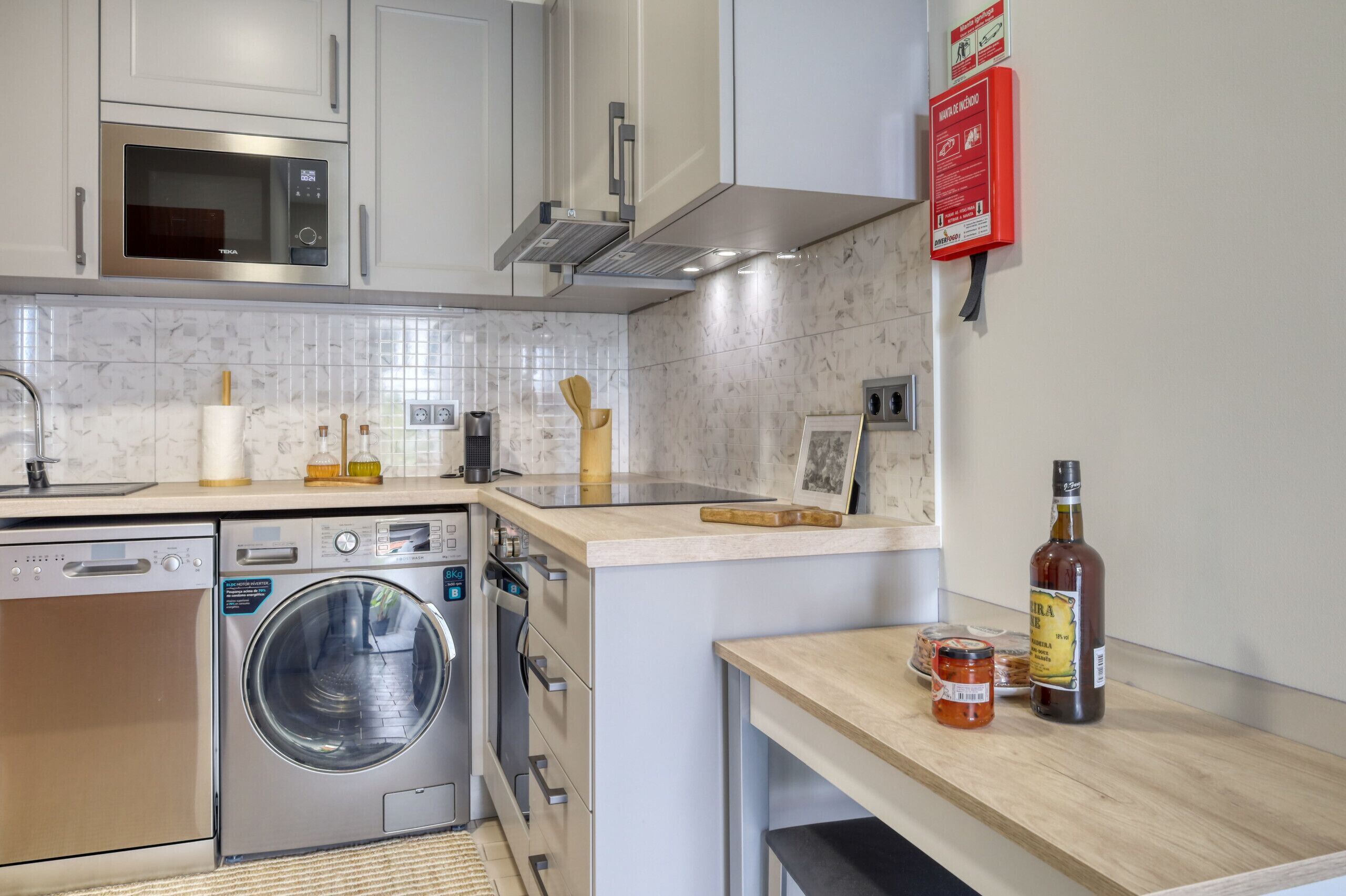 Een moderne keuken met roestvrijstalen apparatuur, een inbouwoven en een magnetron. Er zijn twee spoelbakken, een koffieapparaat en een wijnfles op het aanrecht.
