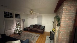 A living room with a Christmas tree, leather sofa, and a fireplace with a brick wall.