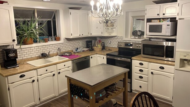 A kitchen with white cabinets, a stainless steel stove, a microwave, a sink, and a chandelier.
