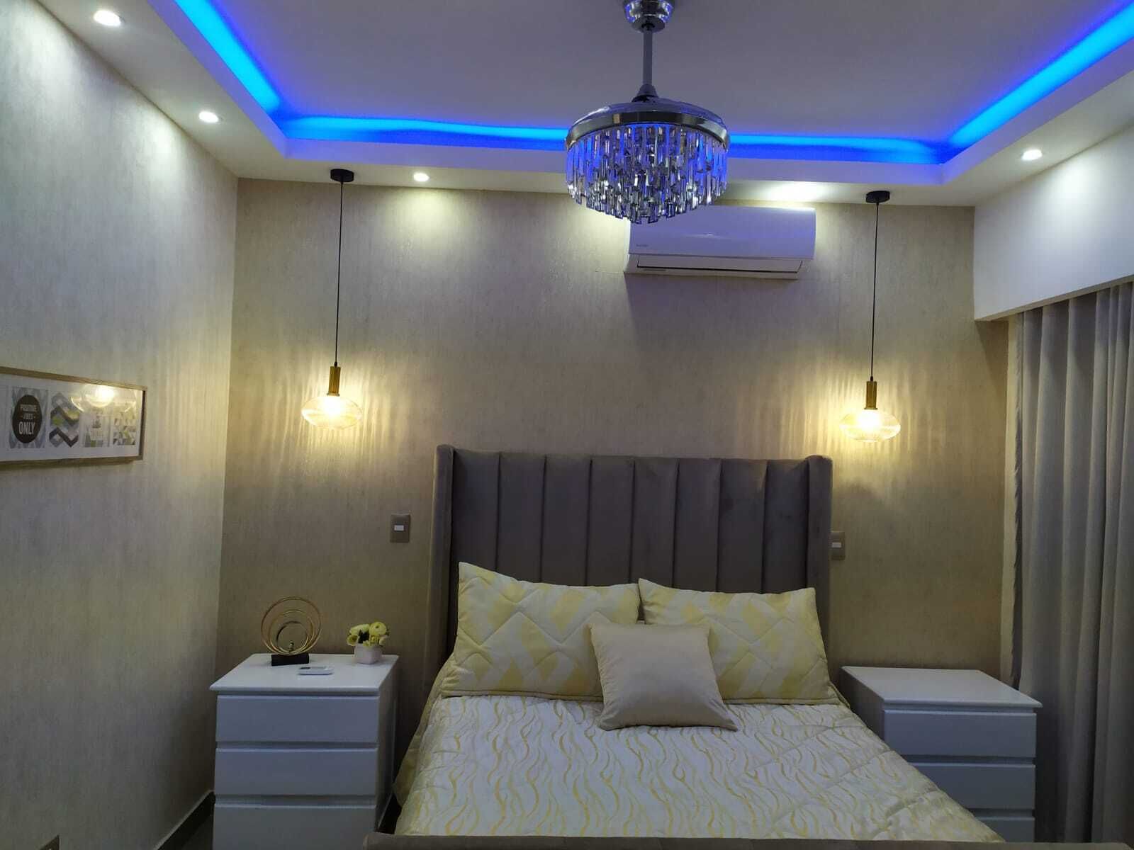 A modern bedroom with a large bed, bedside tables, a chandelier, and wall-mounted lighting.
