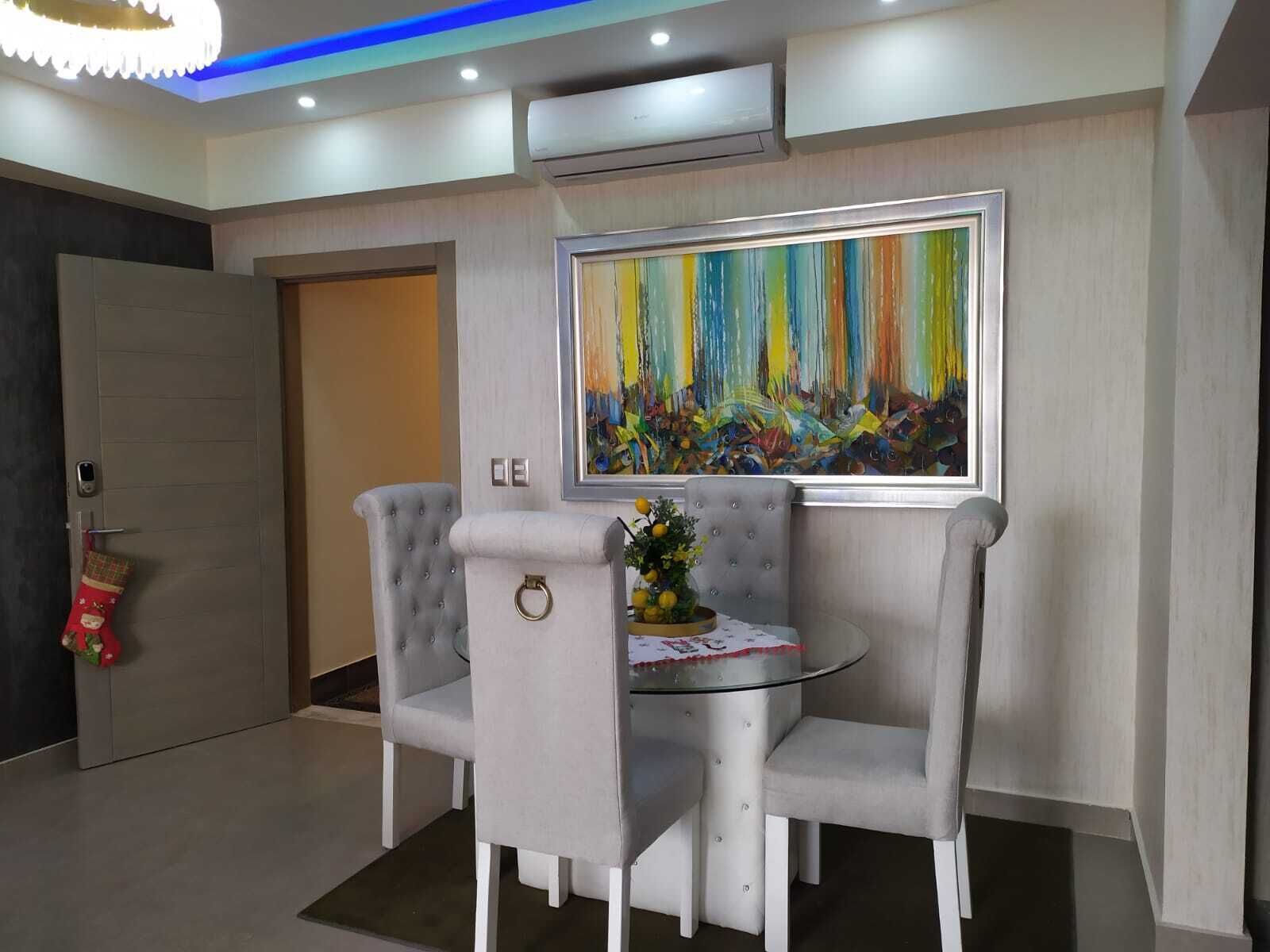 A modern dining area with a glass table, grey upholstered chairs, and a colorful abstract painting on the wall.