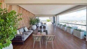 A modern outdoor lounge area with a sofa, chairs, and a dining table, featuring a city view and potted plants. - GOISTAY ROMANTICA VISTA A LAS MONTAÑAS (Santo Domingo)