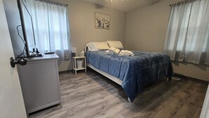 Une chambre à coucher comprenant un lit, un bureau, une chaise, un ventilateur de plafond et une fenêtre avec des rideaux.