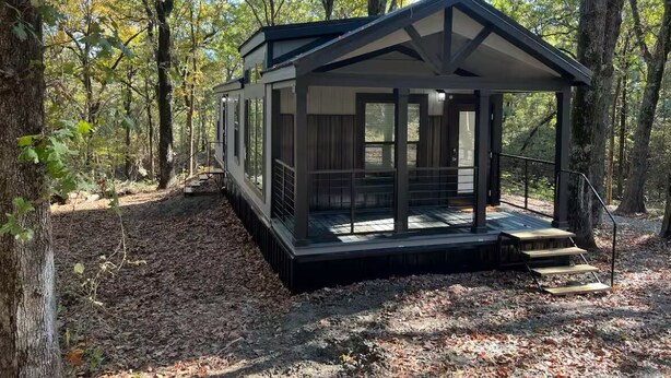 A cabin with a glass enclosure, a deck, and a forested backdrop.