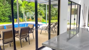 A modern outdoor seating area with a pool, glass doors, and a view of a lush garden. - Large Modern 3-BED house with pool, AC and WiFi in Uvita (Uvita)
