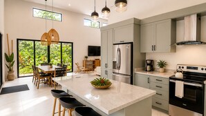 A modern kitchen with a large island, bar stools, stainless steel appliances, and a dining area with natural light. - Large Modern 3-BED house with pool, AC and WiFi in Uvita (Uvita)