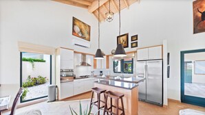 Een moderne keuken met een centraal eiland, roestvrijstalen apparatuur en hangende lampen.