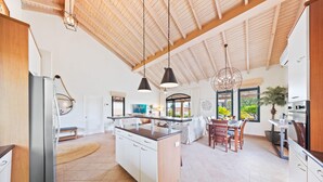 Een ruime keuken met een centraal eiland, houten balken in het plafond, hanglampen, en een eetgedeelte met uitzicht op de omgeving.