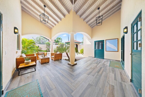 A spacious covered patio with wooden furniture, a central column, and a view of the outside.