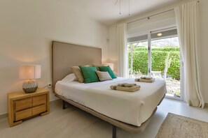Une chambre moderne avec un grand lit, une table de chevet avec une lampe et une vue sur la verdure par la fenêtre.