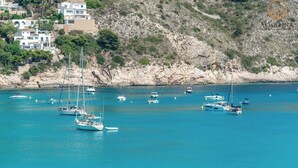 A coastal area with boats anchored in clear blue waters, surrounded by rocky terrain and residential buildings. - Moraira Bay 6 - By Almarina Villas (MORAIRA)
