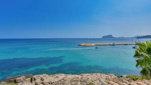 A coastal view with clear turquoise waters, a rocky shoreline, and a distant mountain range. - Moraira Bay 6 - By Almarina Villas (MORAIRA)