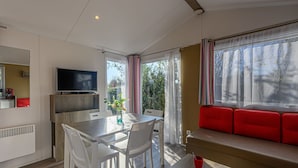 A modern room with a dining table, chairs, a TV, a red sofa, and a window with curtains. - Le Tadorne by Interhome (Carnac)
