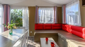 A cozy room with a wooden table, two red chairs, a red sofa, and a window with striped curtains. - Le Tadorne by Interhome (Carnac)