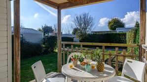 A covered patio with a round table, two white chairs, and a wooden fence. - Le Courlis by Interhome (Carnac)