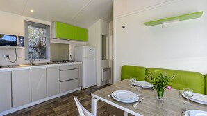 A modern kitchen with white cabinets, a green countertop, and a dining area with a wooden table set for two. - Le Courlis by Interhome (Carnac)