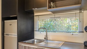 Cocina compacta con pileta integrada, estufa y ventana con persianas.