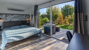 Un dormitorio moderno con una cama grande, un ventanal corredero a una terraza y vista a un jardín.