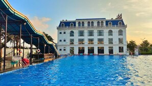 A large swimming pool with a covered area and a building with multiple windows and balconies in the background. - Adamo Hotel Hung Yen (Yen My)