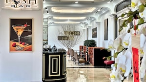 A bar area with a sign reading "LUSH BAR," a framed artwork of a martini glass, and a black and gold bar counter. - Adamo Hotel Hung Yen (Yen My)