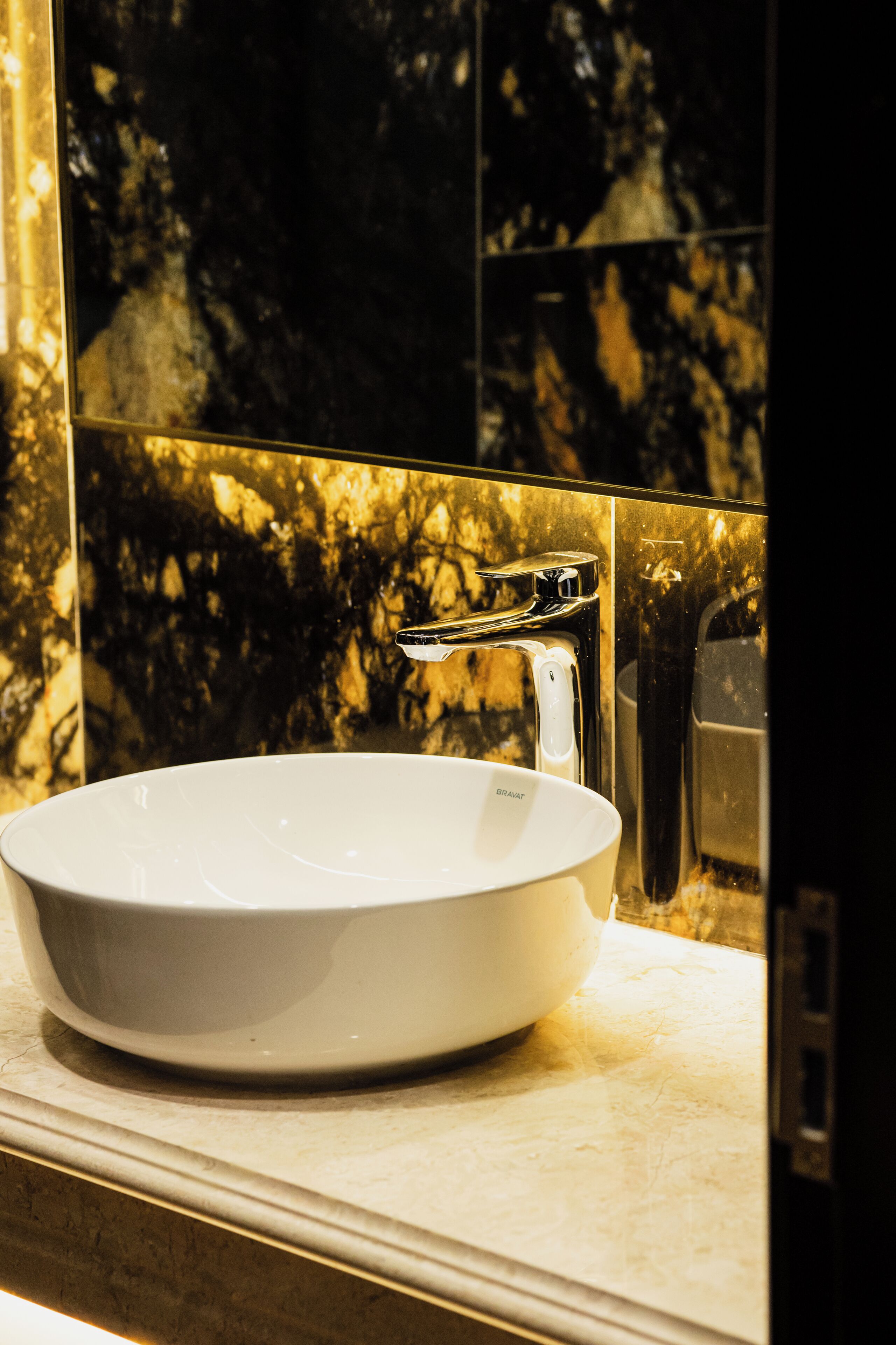 A white ceramic sink with a chrome faucet in a bathroom with marble walls and a mirror.