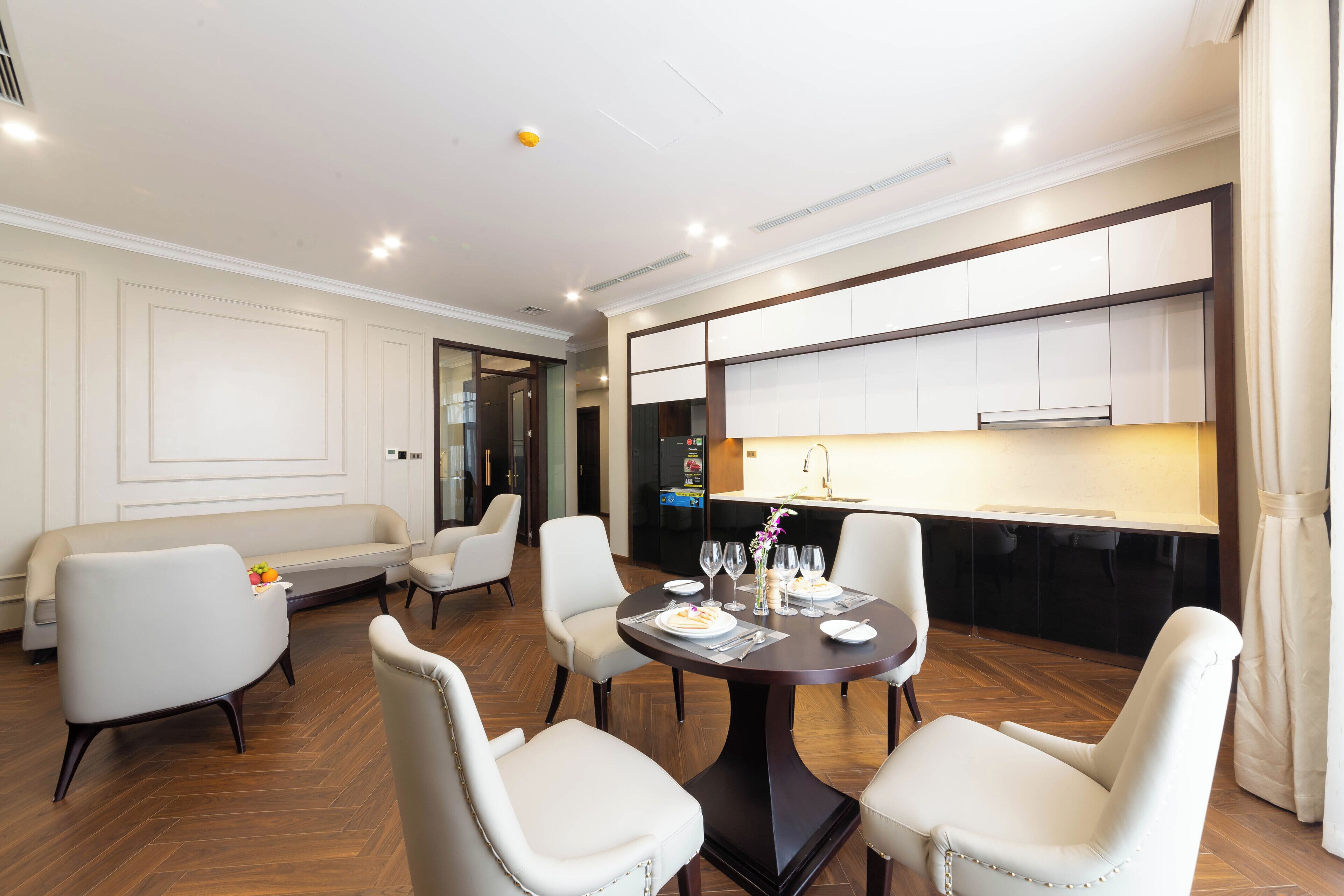 Un comedor moderno con una mesa redonda, sillas blancas y una cocina al fondo.