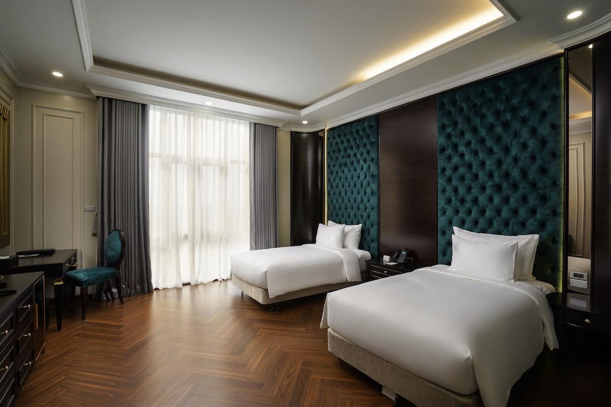 A hotel room with two beds, a desk, a chair, and a large window with curtains.
