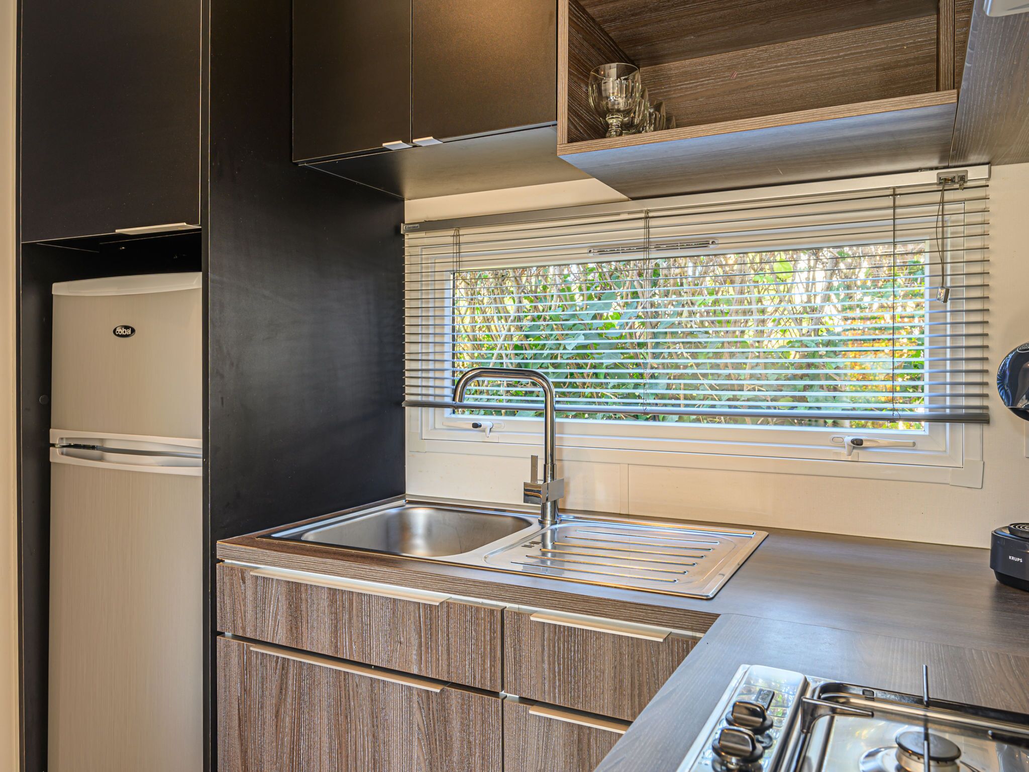 A compact kitchen with a built-in sink, a stove, and a window with blinds.