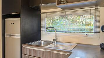 A compact kitchen with a built-in sink, a stove, and a window with blinds.