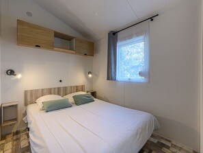 Un dormitorio con una cama, dos mesitas de noche, un estante en la pared, una ventana con cortina y un reloj de pared.