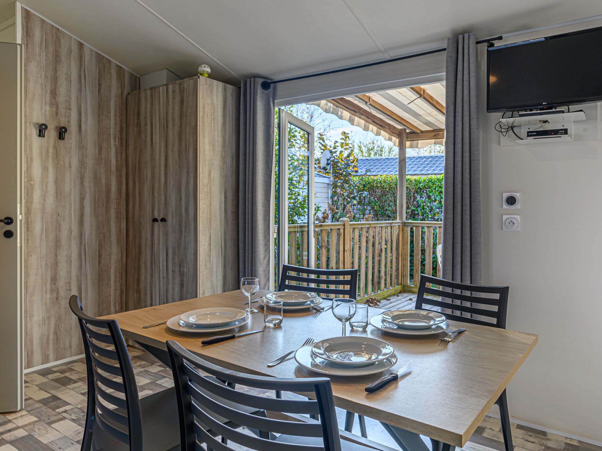 A dining area with a wooden table set for four, chairs, and a TV mounted on the wall.