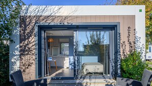 Eine moderne Terrassenausstattung mit Korbmöbeln, einem kleinen Tisch und Blick in ein Schlafzimmer mit Bett und Fenster.