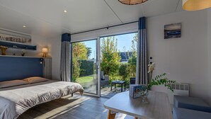 Ein modernes Schlafzimmer mit einem großen Bett, einem Essbereich mit Tisch und Stühlen und einer Glastür, die zu einem Garten führt.