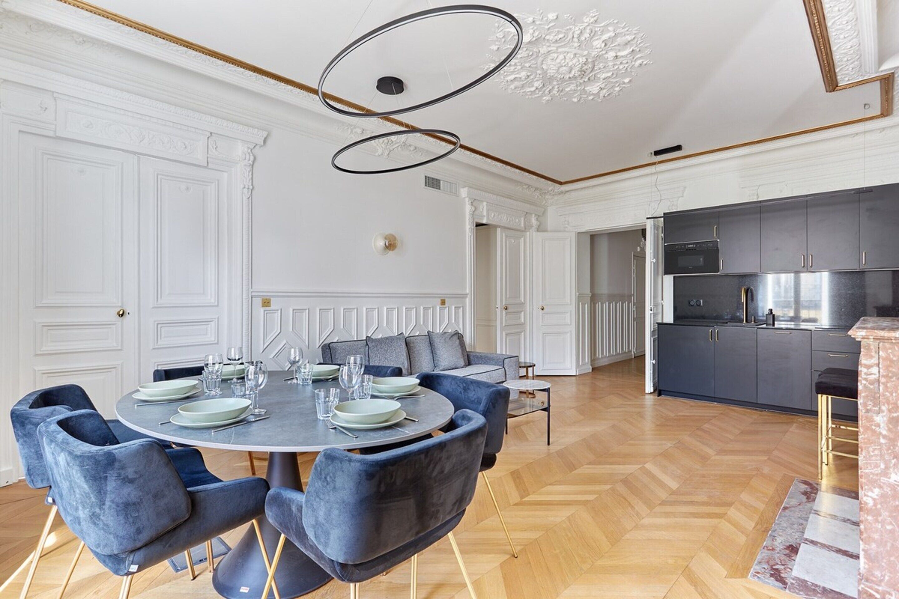A dining area with a round table set for six, surrounded by six blue upholstered chairs.