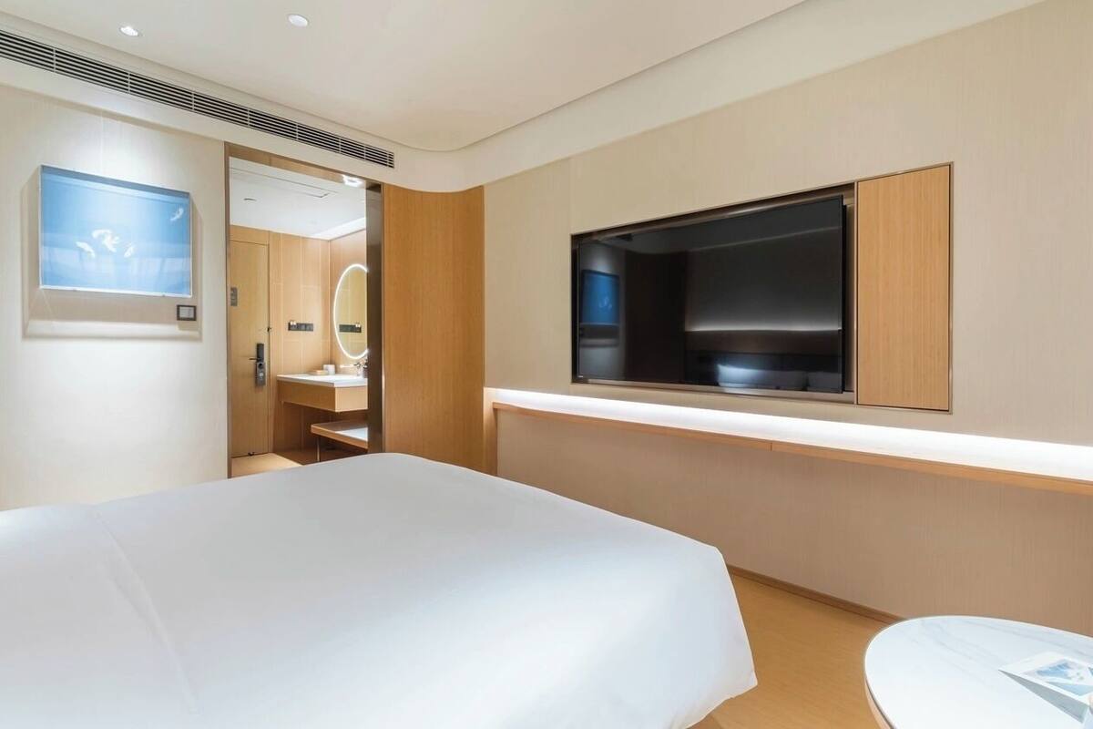 Ein modernes Hotelzimmer mit einem großen Bett, einem an der Wand montierten Fernseher und einem kleinen Tisch.