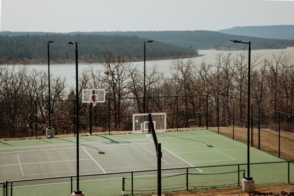 An outdoor basketball court with a net, surrounded by a fence, and overlooking a body of water with trees in the background. - Beck`s Bungalow - Hot Tub|Fire Pit|Heated Pool|Screened Porch (Carlton Landing)