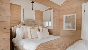 Un dormitorio con techo de madera, una cama con ropa blanca y un cuadro en la pared.