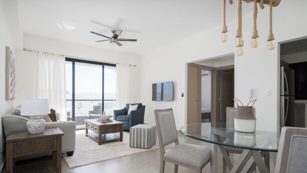 Un salon moderne avec une table à manger en verre, un ventilateur de plafond et une vue sur la ville grâce à de grandes fenêtres.