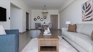 Un salon moderne avec une table basse en bois, un canapé gris et un coin repas agrémenté d’un lustre.